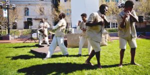 To the beat of Vernon Mobley's drum, the chorus (Chiedu Mbonu and Theophilus Timothy, representing American prisoners, background) and Robben Island inmates (Jamil Joseph and Ryan Fields, foreground) mime hard labor in The Island. 