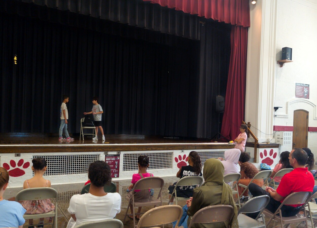 Students performing a scene onstage for a seated audience